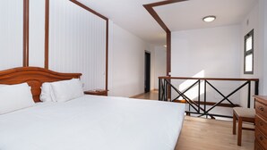 Un dormitorio con cama de madera, mesita de noche, cómoda y balcón con barandilla.