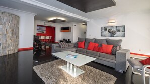 Una sala de estar moderna con un sofá gris, cojines rojos, una mesa de centro blanca y un cuadro abstracto grande en la pared.