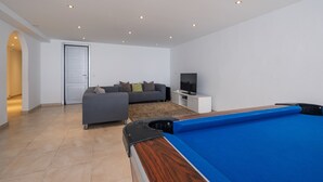 Una sala de estar moderna con una mesa de billar, un sofá, un televisor e iluminación empotrada en el techo.