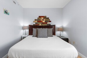Ein ordentlich bezogenes Bett mit weißer Decke und zwei Kissen, umrahmt von zwei Nachttischen mit Lampen, in einem Zimmer mit einem dekorativen Wandbild über dem Bett.