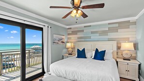 Ein Schlafzimmer mit einem großen Bett, zwei Nachttischen inklusive Lampen, einem Deckenventilator, Meerblick und einem Balkon mit Geländer.