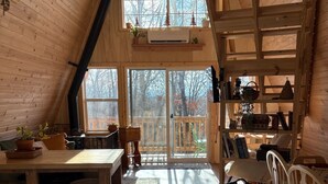 A cozy cabin interior with a loft bedroom, wooden floors, and a dining area with a view of the outdoors. - A Frame Cabin In The Woods (Omaha)