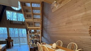 A cozy dining area with a wooden table and chairs, a patterned rug, and a bookshelf. - A Frame Cabin In The Woods (Omaha)