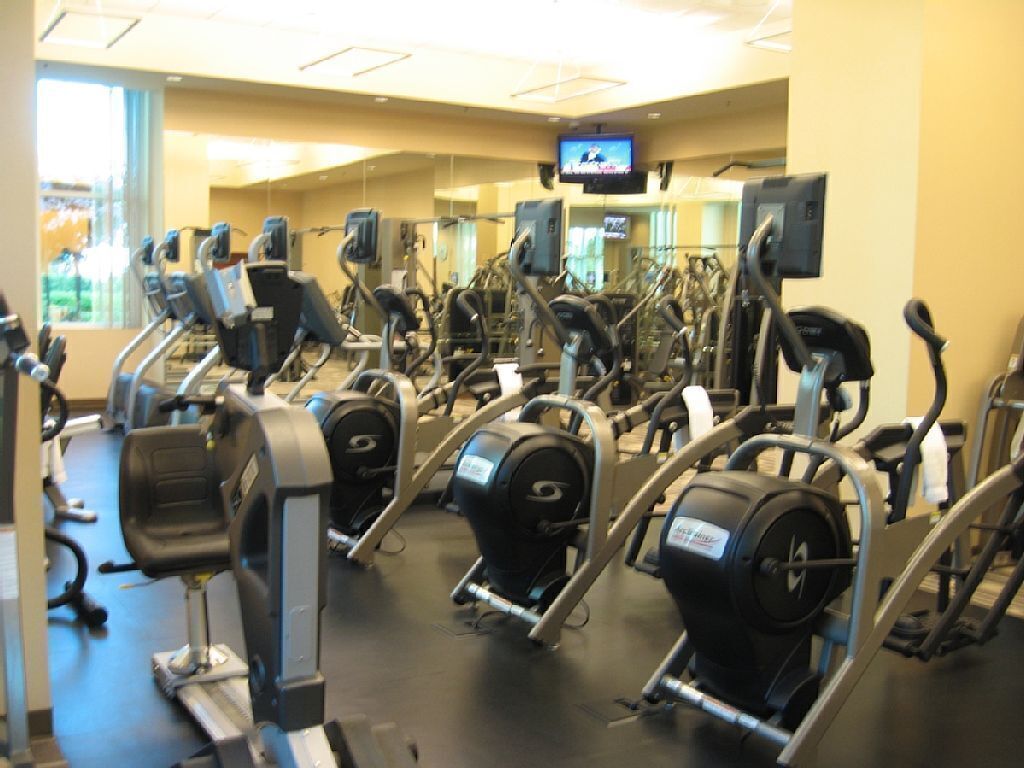 Une salle de sport équipée de divers appareils de cardio, de miroirs et d’un écran de télévision.