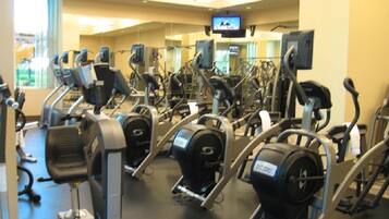 Une salle de sport équipée de divers appareils de cardio, de miroirs et d’un écran de télévision.