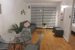 Un salon moderne avec une table à manger en verre, des canapés gris et une plante en pot.