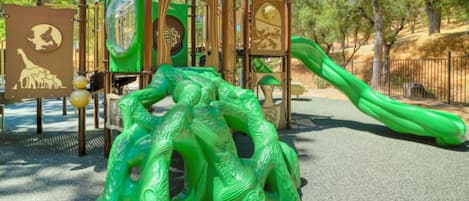 Une aire de jeux avec un toboggan vert et des structures d’escalade.