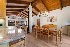 A spacious dining area with a wooden table and chairs, a large window, and a ceiling with exposed beams. - Sunset Ridge at Pine Mountain Lake (Groveland)