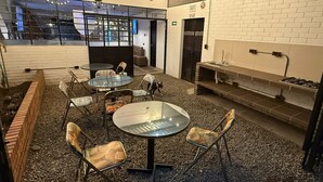 A modern indoor space with round tables and chairs, a brick wall, and a kitchen area. - THE LONDON INN (Bogotá)
