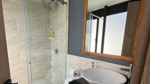 A modern bathroom with a glass shower enclosure, a white toilet, a wooden vanity with a black countertop, and a large mirror above the sink. - THE LONDON INN (Bogotá)