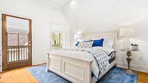 Un dormitorio con una cama blanca, un tapete azul, una puerta de madera y una mesita de noche con una lámpara.