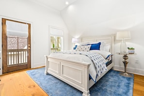 Ein Schlafzimmer mit einem weißen Bett, einem blauen Teppich, einer Holztür und einem kleinen Tisch mit einer Lampe.