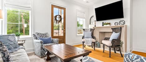 A living room with a wooden coffee table, patterned sofas, a fireplace, and a TV mounted on the wall.