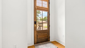 A wooden door with a window, a doormat, and a white wall with a power outlet. - New Luxurious & Elite! Steps to Auburn University & Downtown (Auburn)