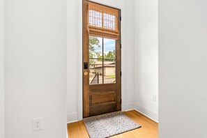 A wooden door with a window, a doormat, and a white wall with a power outlet. - New Luxurious & Elite! Steps to Auburn University & Downtown (Auburn)