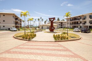 Pátio de hotel com escultura central, palmeiras e um caminho pavimentado.