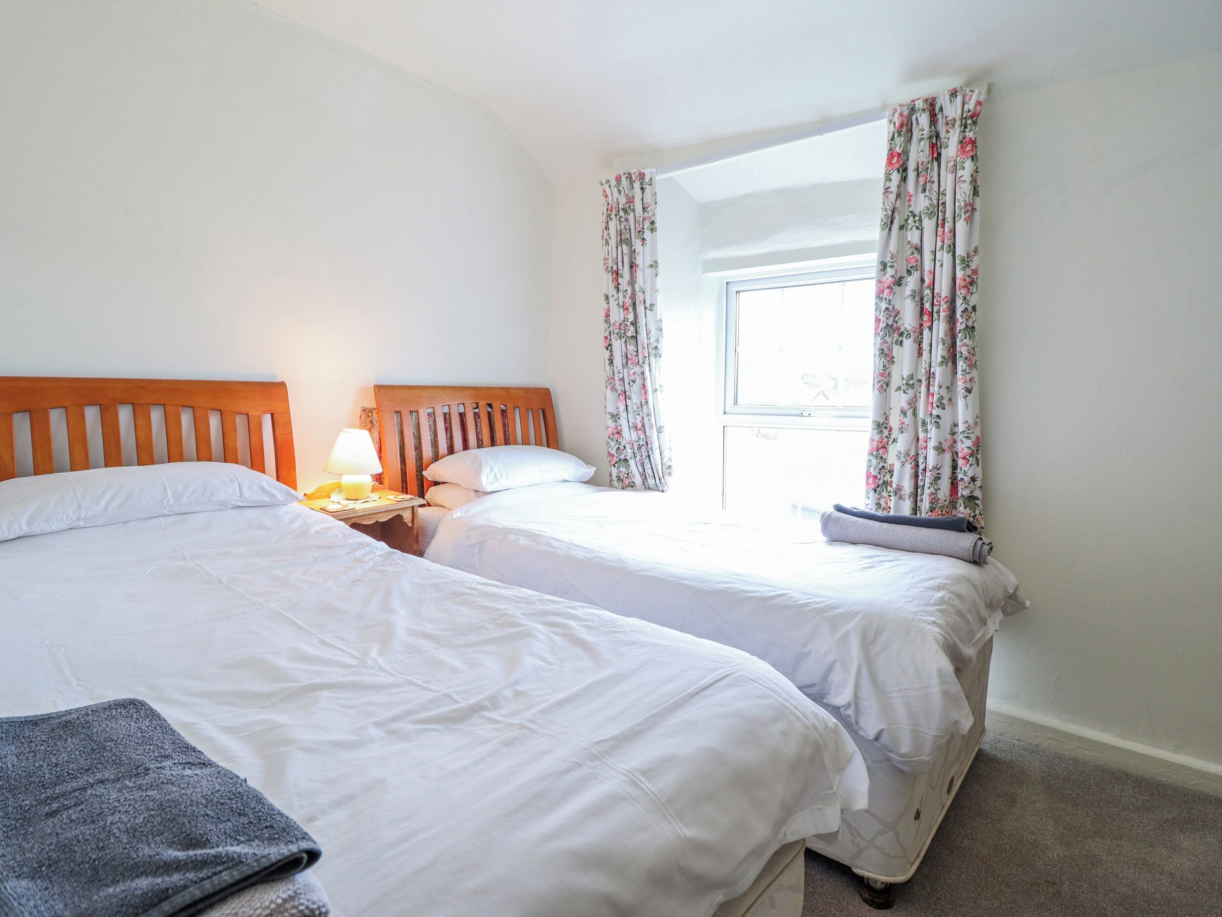 Une chambre avec deux lits, une table de chevet avec une lampe, des rideaux à motifs floraux et une fenêtre.