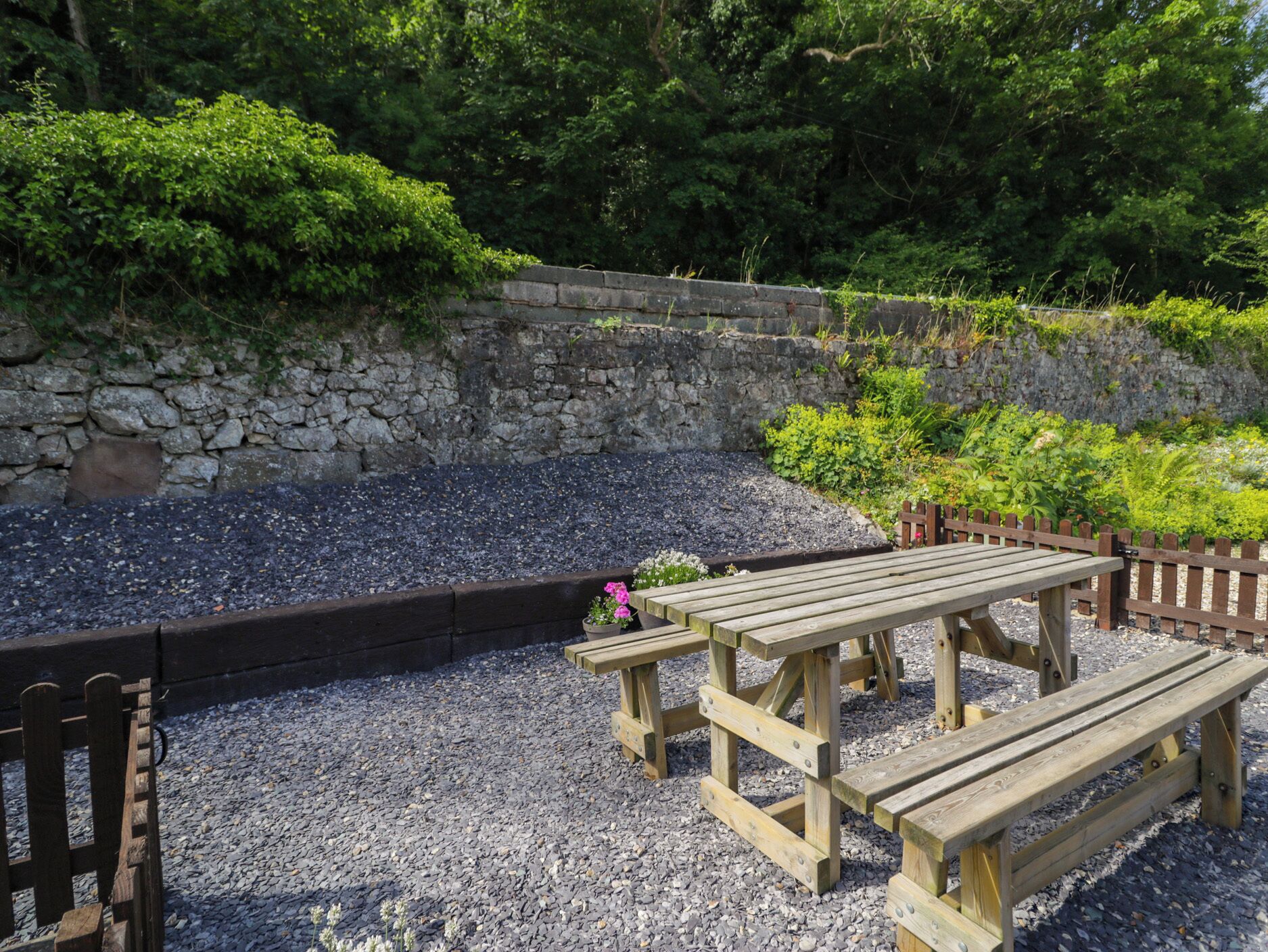 Un espace pique-nique équipé d’une table et de bancs en bois, entouré de gravier et de verdure.