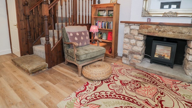 Un salon chaleureux avec un escalier en bois, une cheminée, une bibliothèque et un tapis à motifs.
