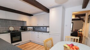 Une cuisine avec des meubles blancs, une cuisinière noire et une table à manger sur laquelle se trouve un panier de fruits.