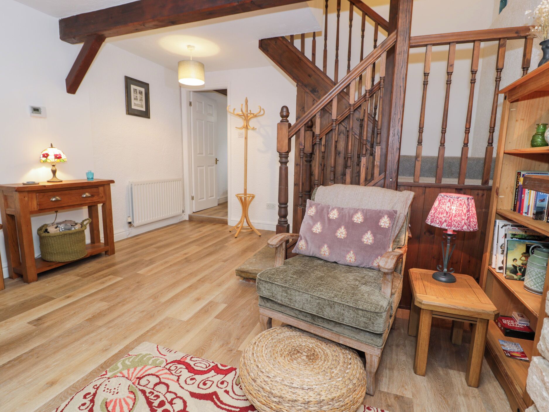 Una sala de estar acogedora con una escalera de madera, un sillón cómodo, una mesita de noche con una lámpara y una estantería.