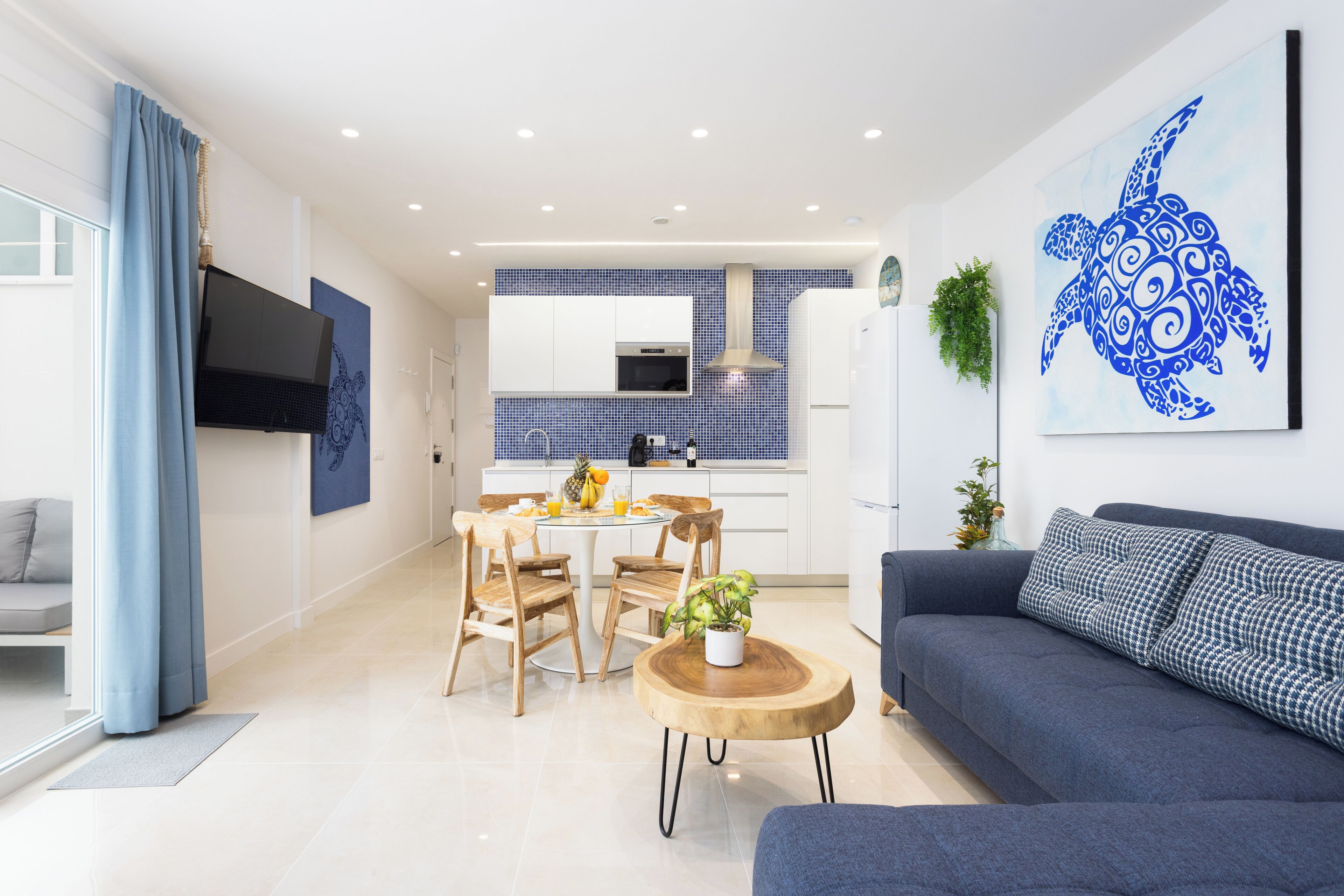 Un espace de vie moderne comprenant un coin repas, une cuisine et une grande œuvre d’art représentant une tortue bleue, accrochée au mur.
