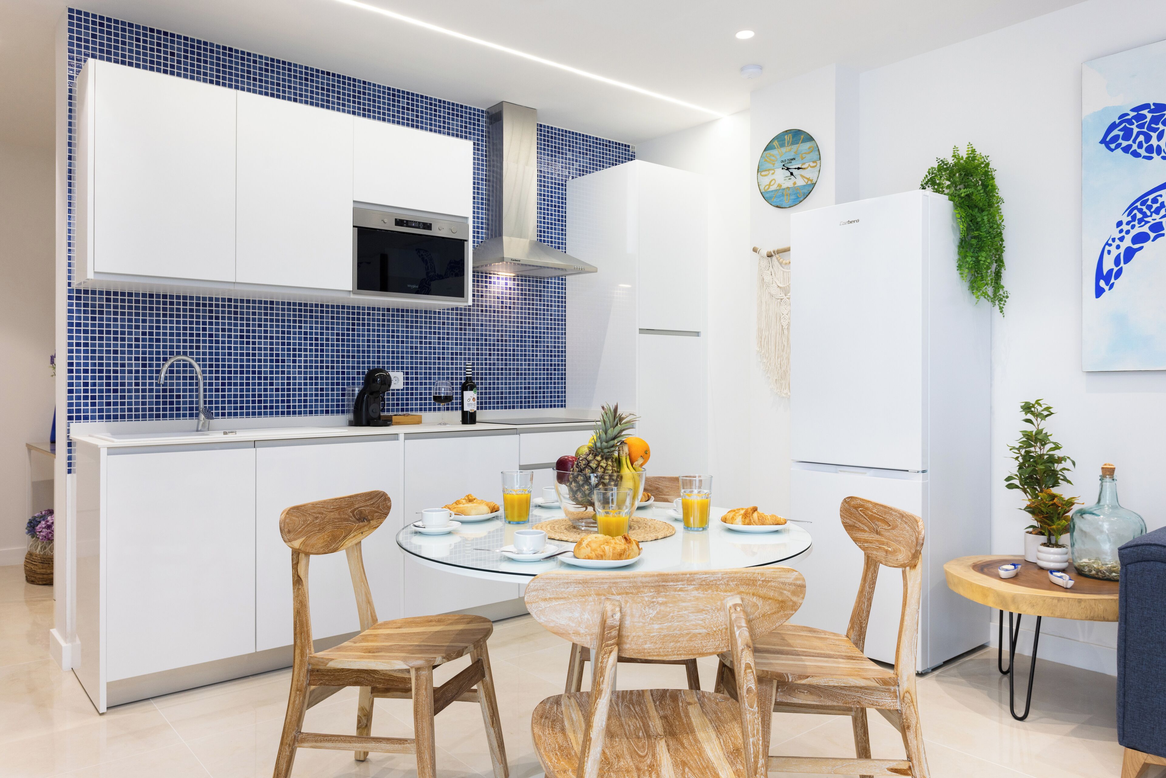 Une cuisine moderne avec des meubles blancs, un pare-feu bleu et un îlot central doté de chaises.