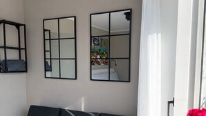 Et moderne værelse med sofa, to vægmonterede spejle og et vindue med lette gardiner.