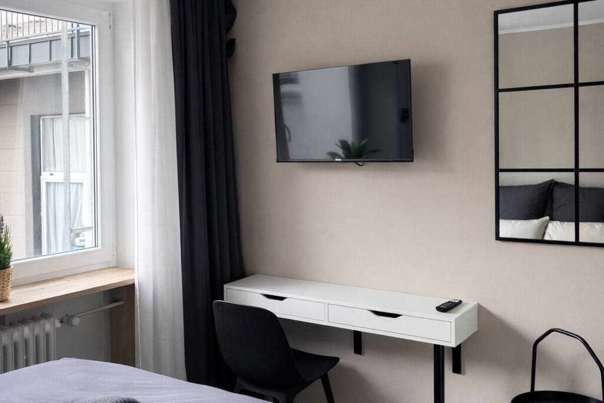 A modern hotel room with a bed, a desk, a chair, a TV, and a window with curtains.