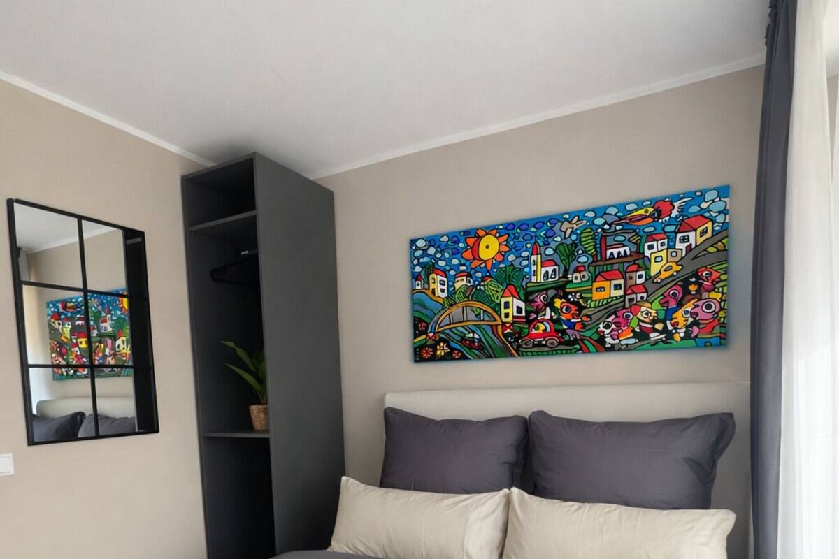 A modern bedroom with a bed, pillows, a painting, a mirror, and a shelf.
