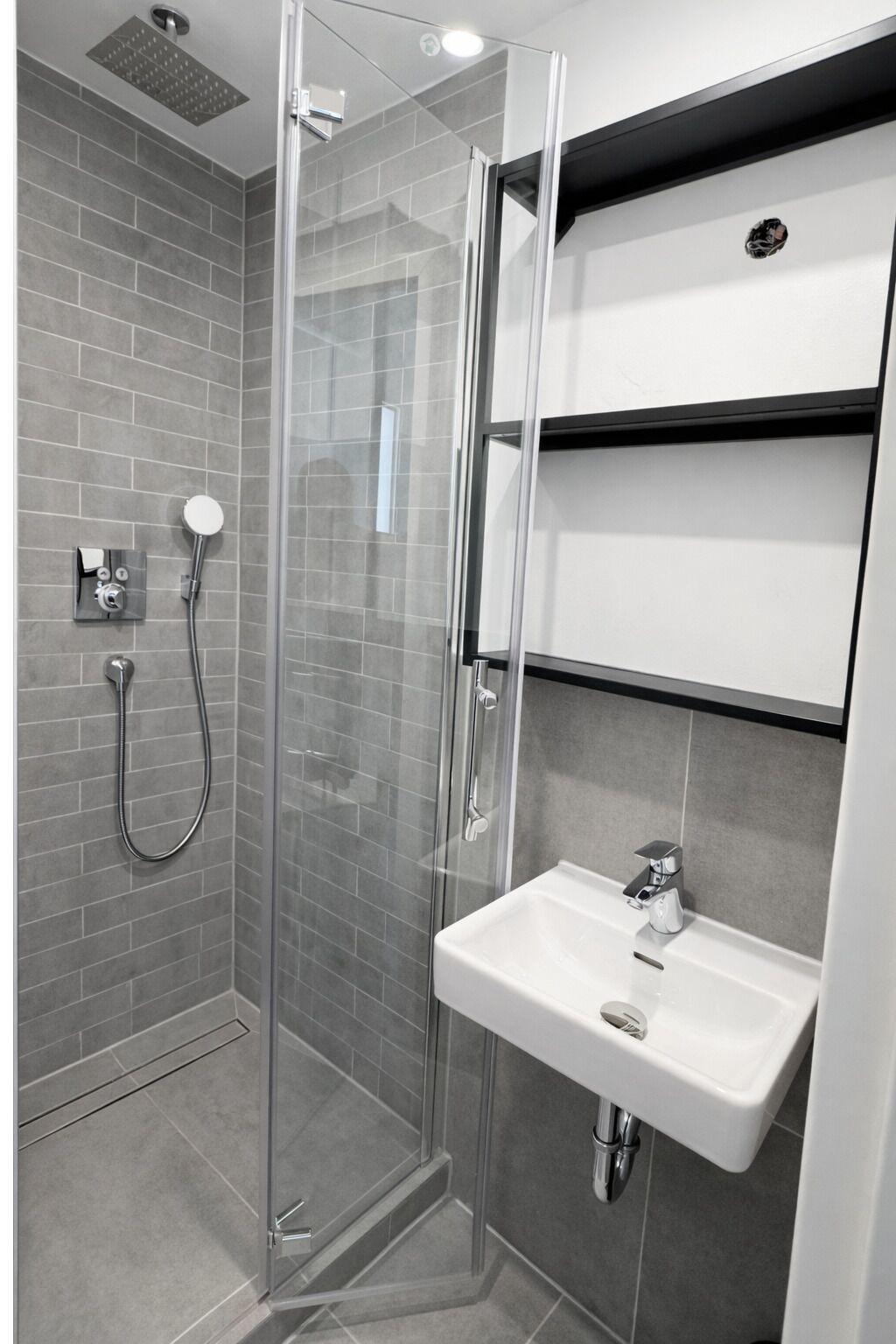 Ein modernes Badezimmer mit einer Duschkabine, einem weißen Waschbecken und einer integrierten Ablagefläche.