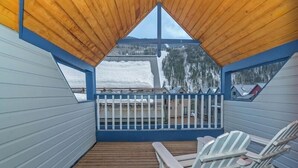 Un terrazzo in legno con poltrone Adirondack bianche, una ringhiera blu e vista su montagne innevate.