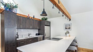 Una cucina moderna con mobili scuri, un piano di lavoro bianco, un'isola integrata e un trave in legno al soffitto.