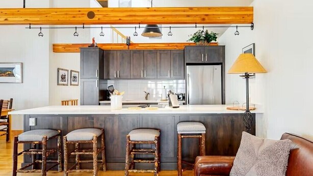 Una cucina moderna con mobili scuri, un frigorifero in acciaio inossidabile e una grande isola con sgabelli da bar.