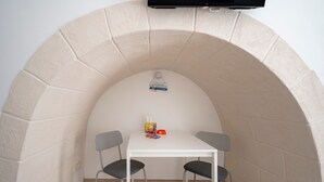 Une petite pièce avec une table blanche et deux chaises, un téléviseur fixé au mur et un sol carrelé.
