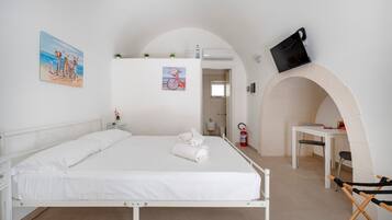 Een slaapkamer met een bed, een klein tafeltje, een stoel, een gewelfde deuropening en een aan de muur bevestigde televisie.