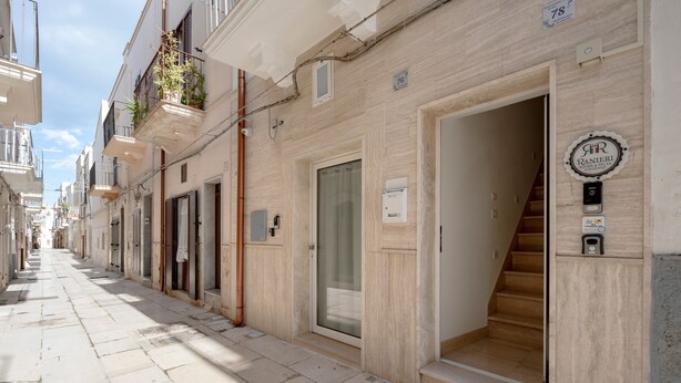 Une rue étroite bordée d’immeubles, une porte bien visible avec une enseigne, et un escalier menant à un étage supérieur.