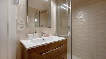 Une salle de bain moderne avec un lavabo blanc, un meuble-lavabo en bois, un grand miroir et une cabine de douche en verre.