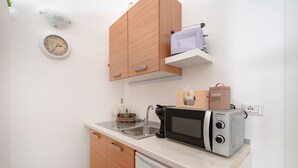 Une cuisine de taille réduite, équipée d’un four à micro-ondes, d’un évier et de meubles de rangement en bois.