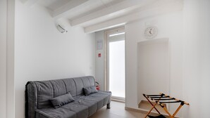 Un moderno salón con un sofá gris, un tendedero de madera y una pared blanca con un reloj.