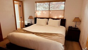 A neatly made bed with a headboard, two bedside tables with lamps, and a window with blinds. - Coffee Pot Trailhead Bungalow, Red Rock Views, Private Patios, Red Rock Pass (Sedona)