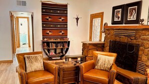 A cozy living room with leather armchairs, a bookshelf, a stone fireplace, and a patterned rug. - Coffee Pot Trailhead Bungalow, Red Rock Views, Private Patios, Red Rock Pass (Sedona)
