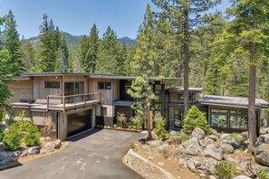 Ein modernes, zweistöckiges Haus mit Garage, eingebettet in eine natürliche Landschaft mit Bäumen und Bergen.