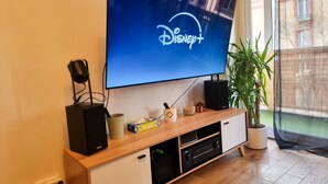 Ein Flachbildfernseher an einem Holz-TV-Möbel montiert, mit einem Lautsprecher und einem kleinen Blumentopf daneben.