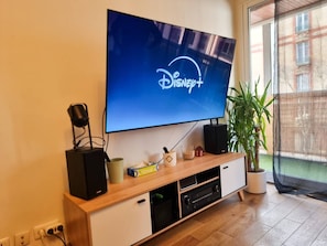 Ein Flachbildfernseher an einem Holz-TV-Möbel montiert, mit einem Lautsprecher und einem kleinen Blumentopf daneben.