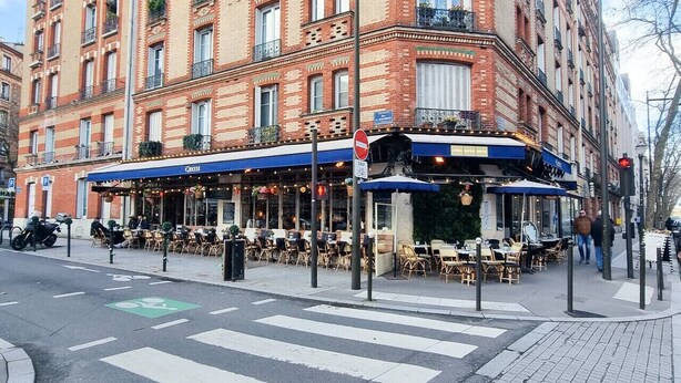Ein Restaurant mit Außenbestuhlung, einer blauen Markise und einer Fußgängerampel.