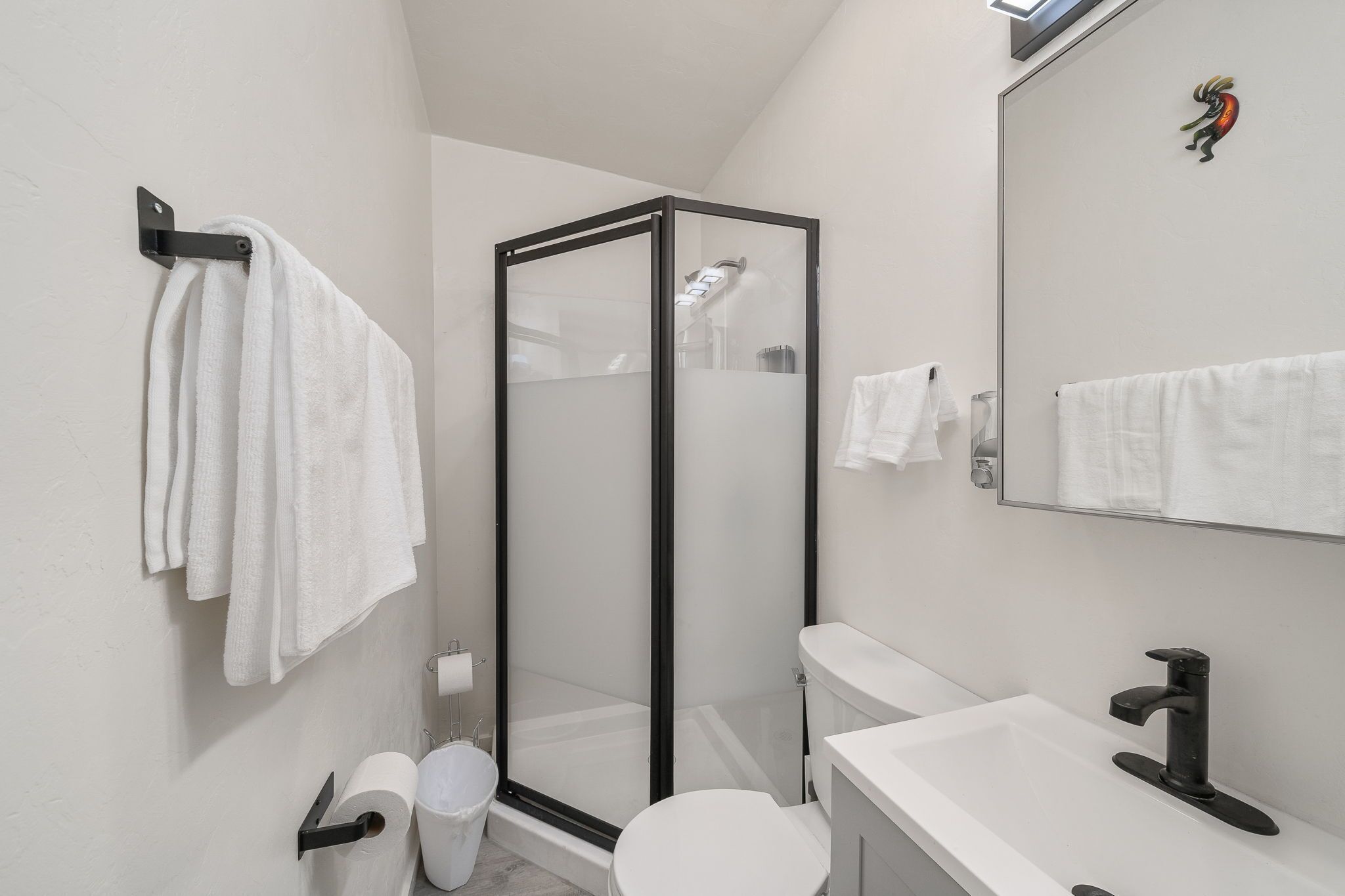 A modern bathroom with a glass-enclosed shower, a toilet, a sink, and a mirror.