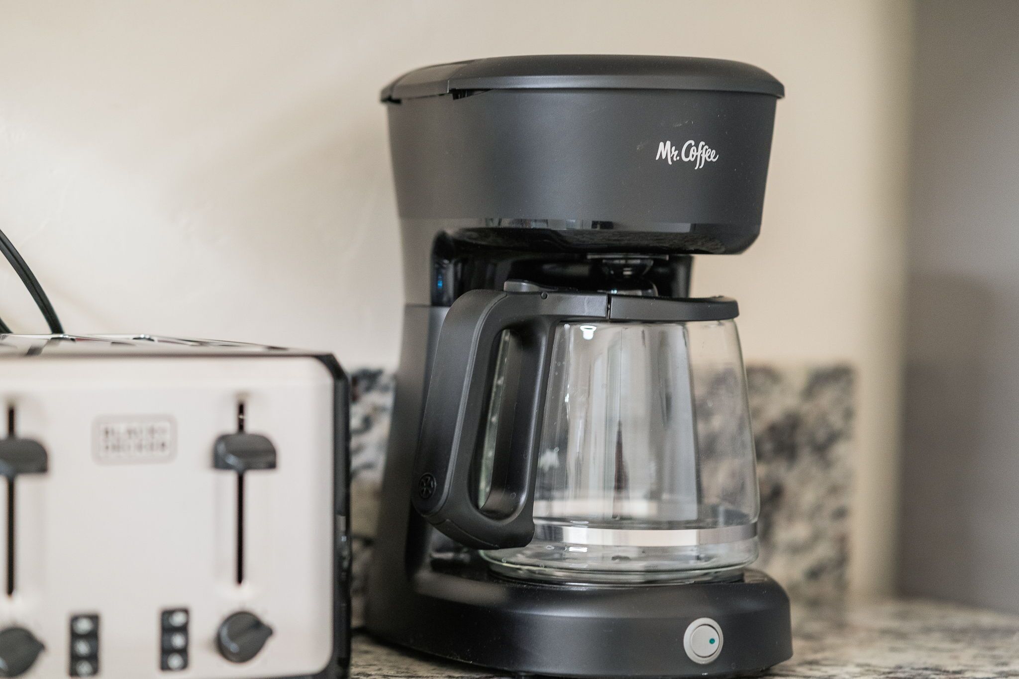 A coffee maker with a clear carafe and a toaster on a countertop.