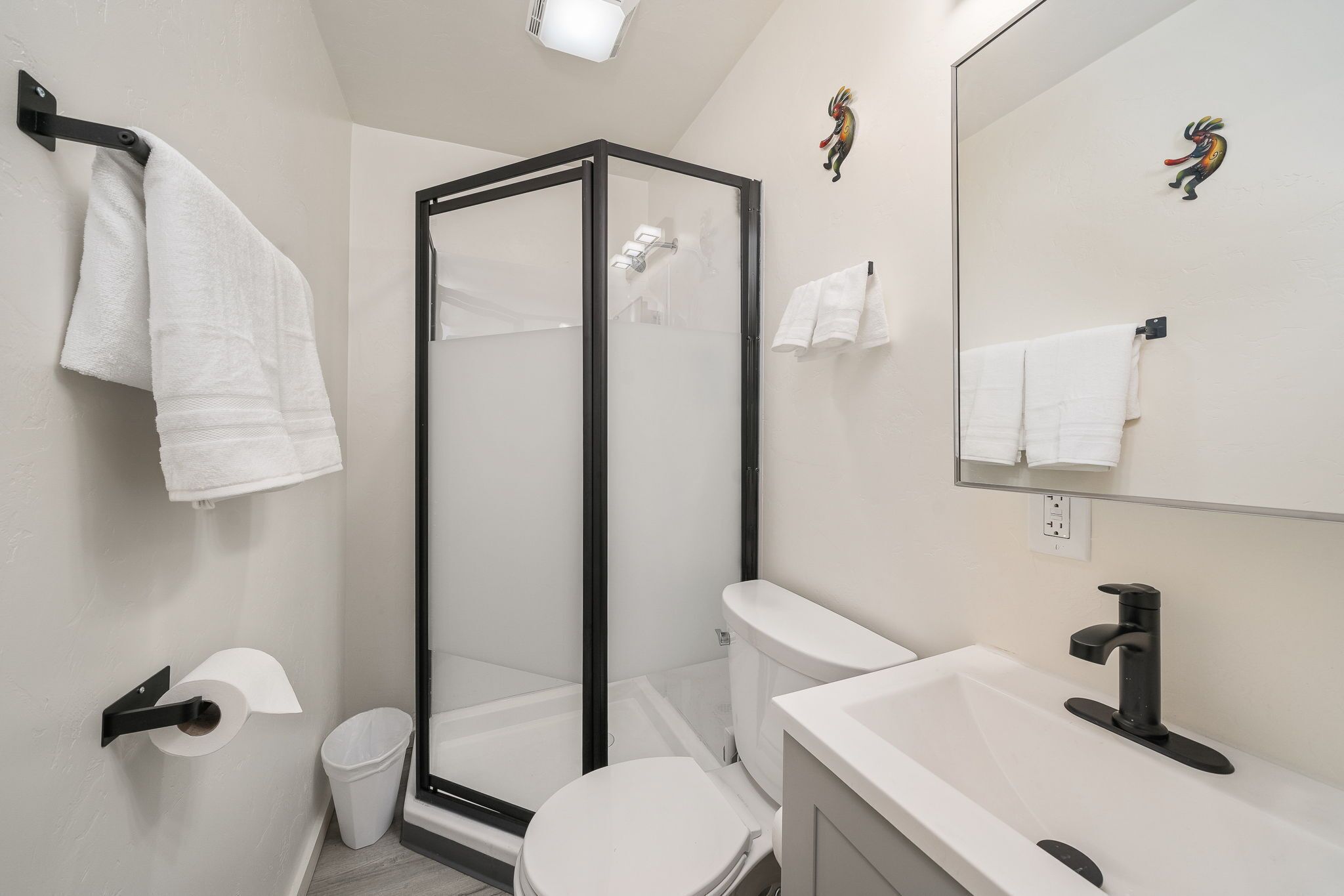 A modern bathroom with a glass-enclosed shower, a white toilet, a sink with a black faucet, and a mirror with a towel rack.