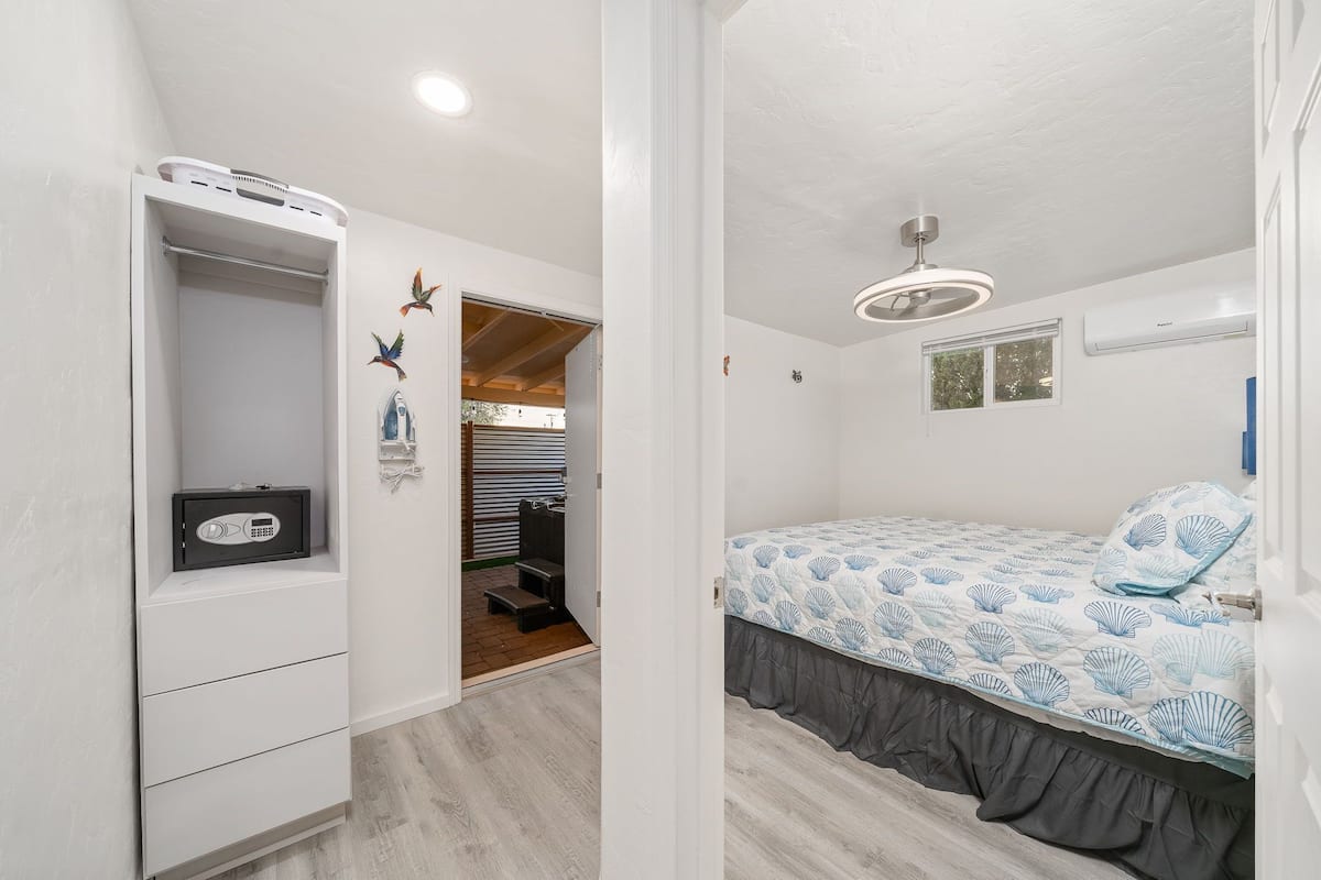 Um quarto com cama, guarda-roupa, aquecedor e ventoinha no teto.
